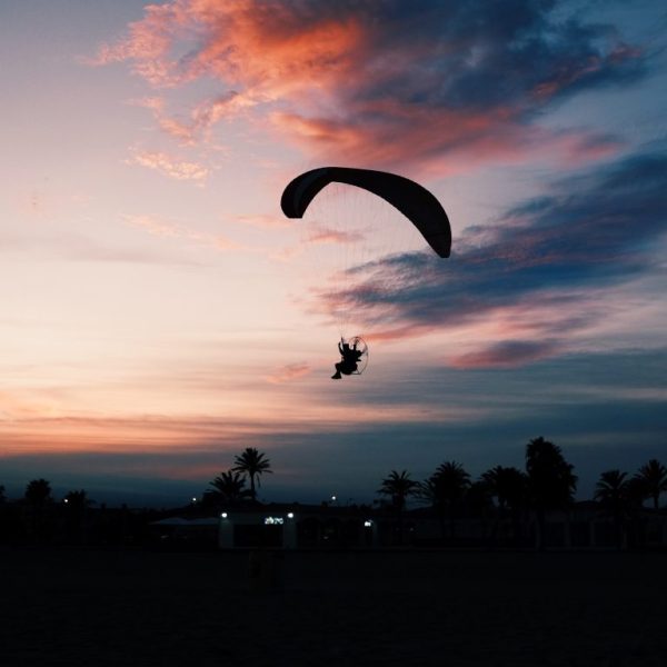 Horizontal shot of a beach with a person gliding down on a paramotor parachute